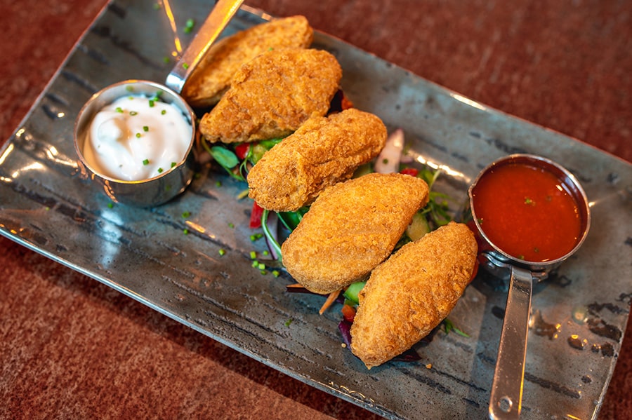 A plate of crispy breaded chicken bites served on a bed of fresh salad, accompanied by two dipping sauces—one creamy and one spicy—on a rustic ceramic plate.